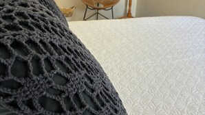 A bed with a white quilted cover and a dark gray crocheted pillow. - Casa Milagres Reserva do toque (São Miguel dos Milagres)