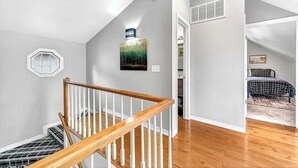 A staircase with wooden railings leading to a landing with a painting and a vent. - The Oak Cottage- Charming Downtown Retreat in the Heart of Siloam Springs (Siloam Springs)