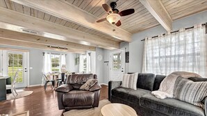 A spacious living room with a dark leather sofa, a wooden coffee table, and a ceiling fan. - The Oak Cottage- Charming Downtown Retreat in the Heart of Siloam Springs (Siloam Springs)