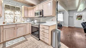 A kitchen with wooden cabinets, a microwave, stove, and a trash can. - The Oak Cottage- Charming Downtown Retreat in the Heart of Siloam Springs (Siloam Springs)