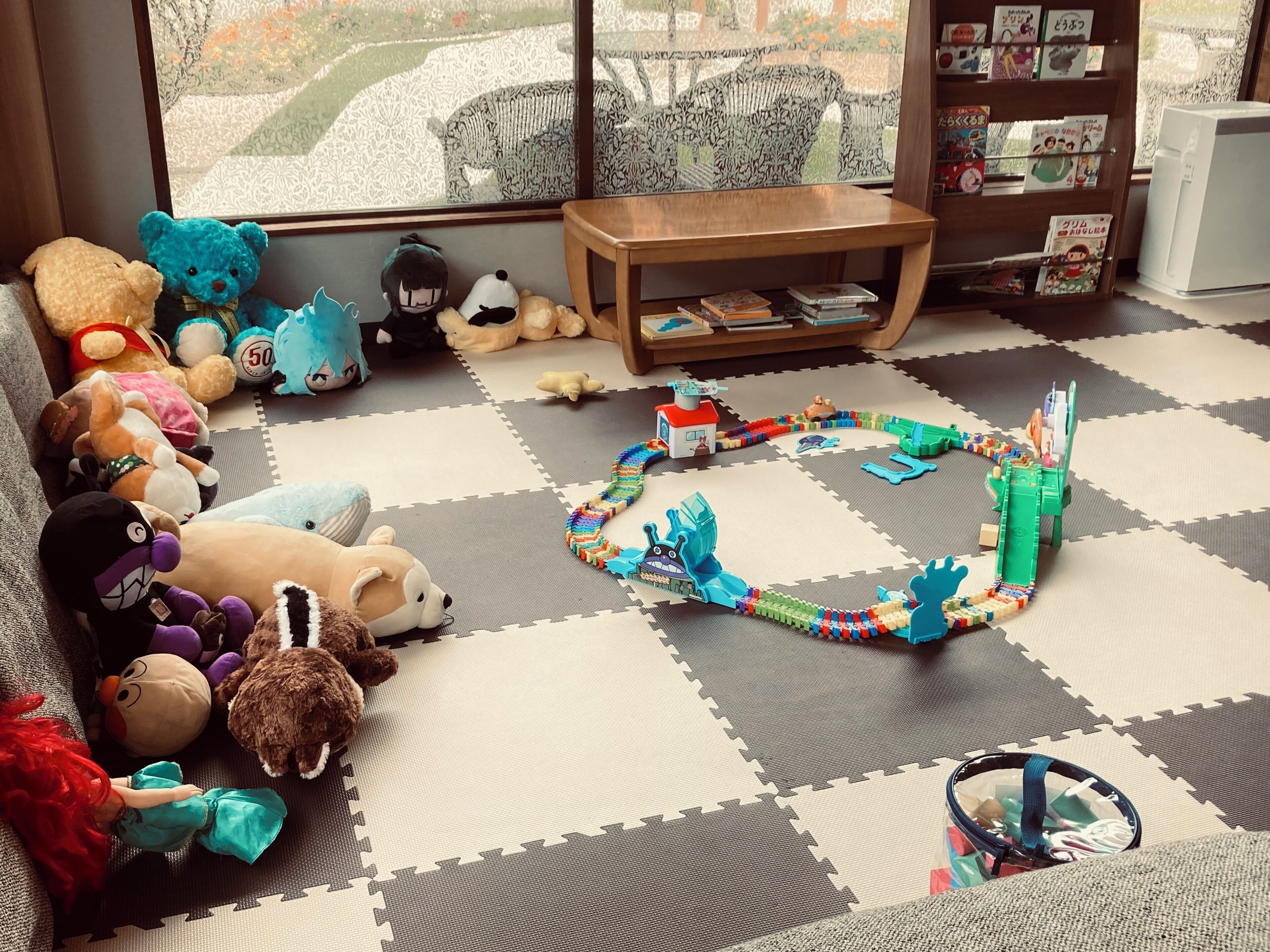 A room with a play area featuring a train set, plush toys, and a bookshelf with books.
