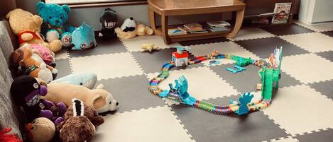 A room with a play area featuring a train set, plush toys, and a bookshelf with books.