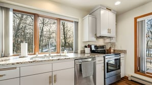 A kitchen with a large window, stainless steel appliances, and white cabinetry. - Contemporary Northwoods Retreat- In the Heart of Sister Bay (Sister Bay)