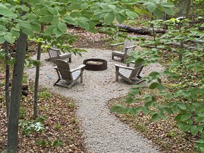 En grussti fører hen til et siddeområde med fire Adirondack-stole og et bålfælleskab i midten.