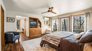 A bedroom with a bed, a ceiling fan, a TV, a wardrobe, a chair, and large windows. - Contemporary Northwoods Retreat- In the Heart of Sister Bay (Sister Bay)
