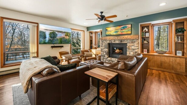 A spacious living room with a stone fireplace, leather sofas, a wooden coffee table, and large windows offering views of trees. - Contemporary Northwoods Retreat- In the Heart of Sister Bay (Sister Bay)