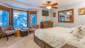 Ein Schlafzimmer mit Bett, zwei Stühlen, einem Schminktisch und einem Deckenventilator, mit großen Fenstern und Blick auf Schnee.