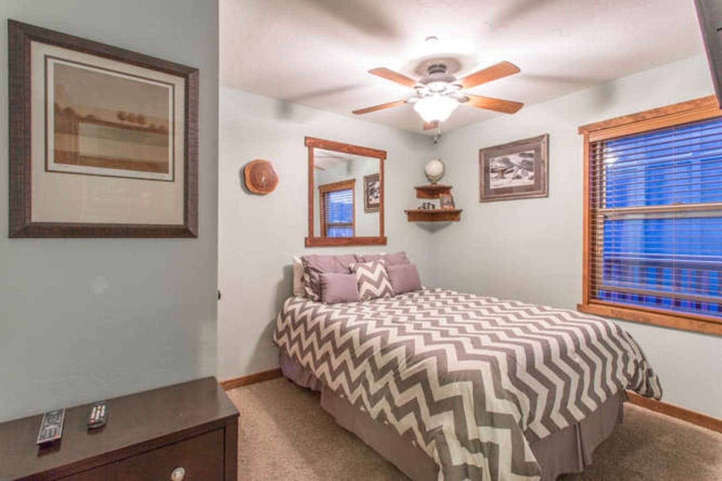 A bedroom with a bed, a ceiling fan, a window with blinds, and a dresser.