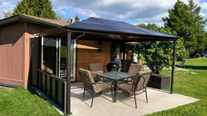 Un patio techado con mesa y sillas, una parrilla y vistas a una casa.