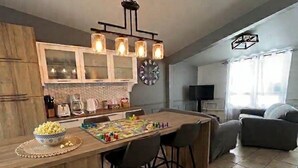 Una cocina moderna con una isla de madera, un área de comedor con sillas, un reloj y un televisor en la sala de estar.