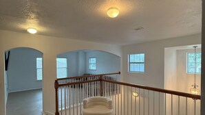 Ein geräumiges Zimmer mit einer Holztreppe, einem weißen Stuhl und Blick durch große Fenster nach draußen.