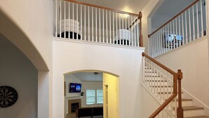 Ein geräumiger, mehrstöckiger Hausinnenraum mit einer Treppe, einem Fernseher im Hintergrund und einer Dartscheibe an der Wand.