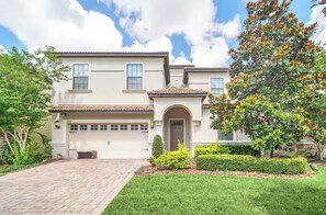 A two-story house with a garage, a brick driveway, and a well-maintained lawn. - Luxury 9BR Villa/ Themed Rooms/ Private Pool/ Game room (Davenport)