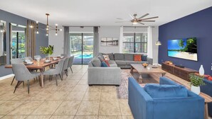 Una sala de estar moderna con comedor, sofás grises, televisor y ventilador de techo.