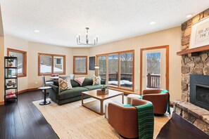 A spacious living room with a fireplace, large windows, a chandelier, and a cozy seating area. - A Wisp-Er Away: 5BR retreat at Wisp,hot tub & fire pit, Ski, Golf (McHenry)