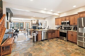 A spacious kitchen with wooden cabinets, a stone tile floor, and modern appliances. - A Wisp-Er Away: 5BR retreat at Wisp,hot tub & fire pit, Ski, Golf (McHenry)