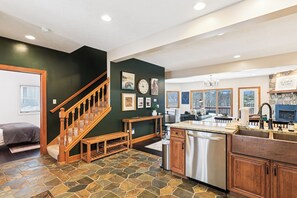 A modern kitchen with a stone floor, wooden staircase, and a stone fireplace. - A Wisp-Er Away: 5BR retreat at Wisp,hot tub & fire pit, Ski, Golf (McHenry)