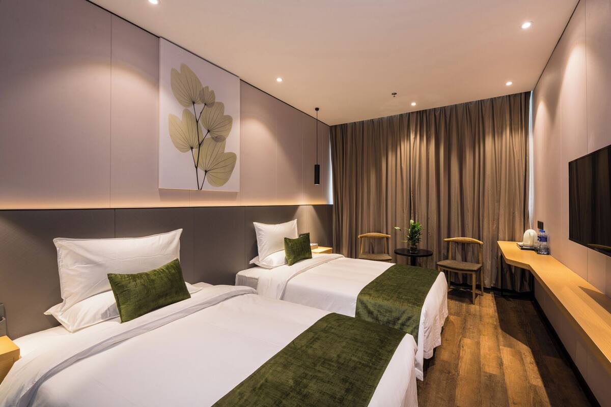 A hotel room with two beds, a desk, a chair, a television, and a large window with curtains.