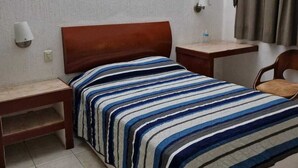 A single bed with a striped bedspread, two bedside tables, a nightstand, a lamp, a chair, and a curtain.