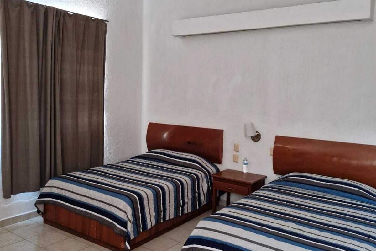 A hotel room with two beds, a ceiling fan, a nightstand, a wall-mounted shelf, and a window with curtains.