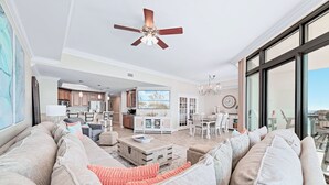 A spacious living room with a large sofa, a dining area, and a kitchen in the background. - The Oasis 1804 | Beautiful, spacious, beach front condo! Endless Amenities! (Orange Beach)