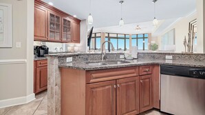 A modern kitchen with granite countertops, wooden cabinets, and a dishwasher. - The Oasis 1804 | Beautiful, spacious, beach front condo! Endless Amenities! (Orange Beach)