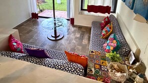 Ein Zimmer mit Glastisch, gepolstertem Sofa mit Muster, Blick auf Boote durch eine Schiebetür und Fliesenboden.