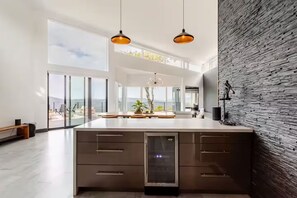 Eine moderne Küche mit Kochinsel, großen Fenstern und Blick ins Freie.