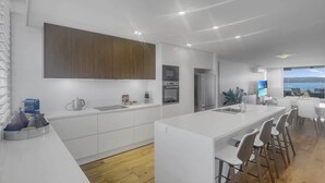 Een moderne keuken met een centraal eiland, een eethoek met stoelen en uitzicht op zee.