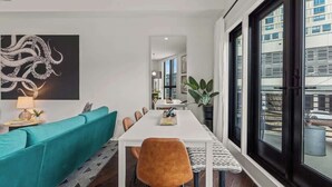 Un comedor moderno con una mesa blanca, sofá azul turquesa y un ventanal con vistas a edificios.