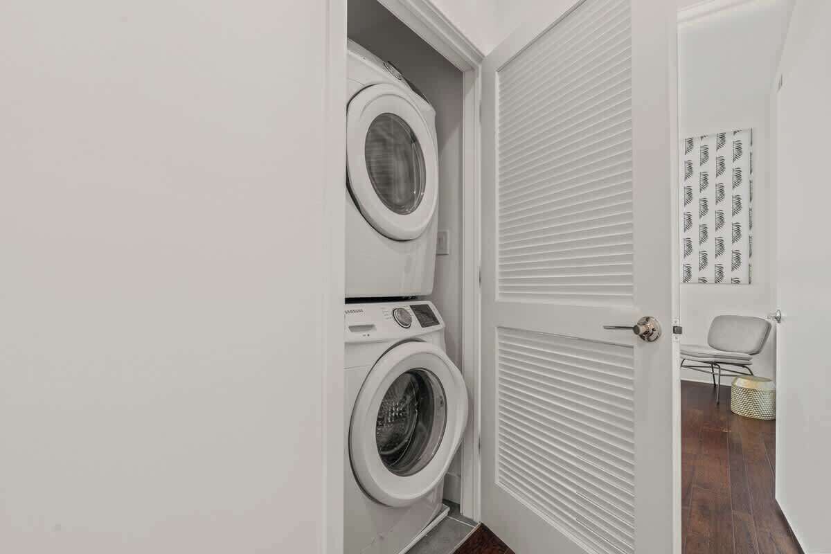 A laundry room with two stacked washing machines, a door with a patterned design, and a chair.