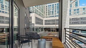 Un balcón con una zona de estar, vistas a un estacionamiento y edificios modernos al fondo.
