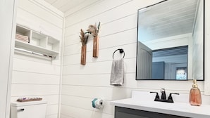 A bathroom with a white toilet, a vanity with a mirror, and a shelf with towels.