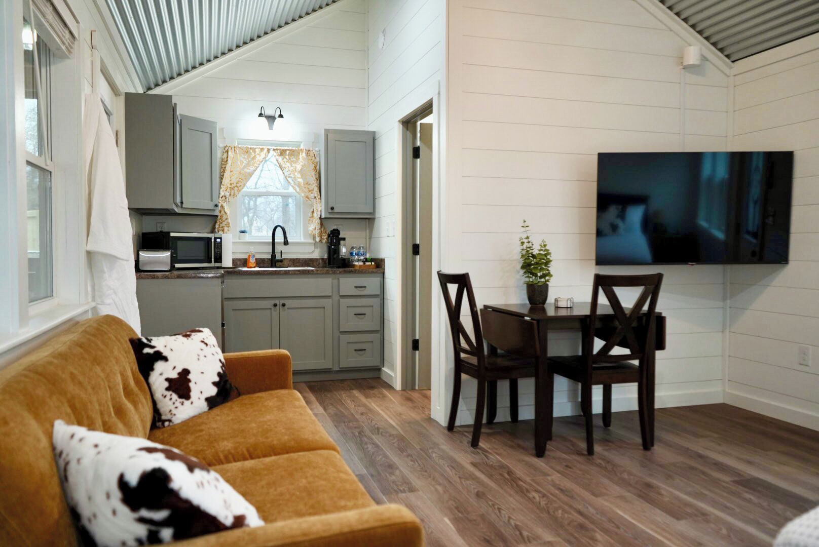 A compact living space with a sofa, dining table, chairs, a TV, and a kitchen area.