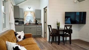 A compact living space with a sofa, dining table, chairs, a TV, and a kitchen area.