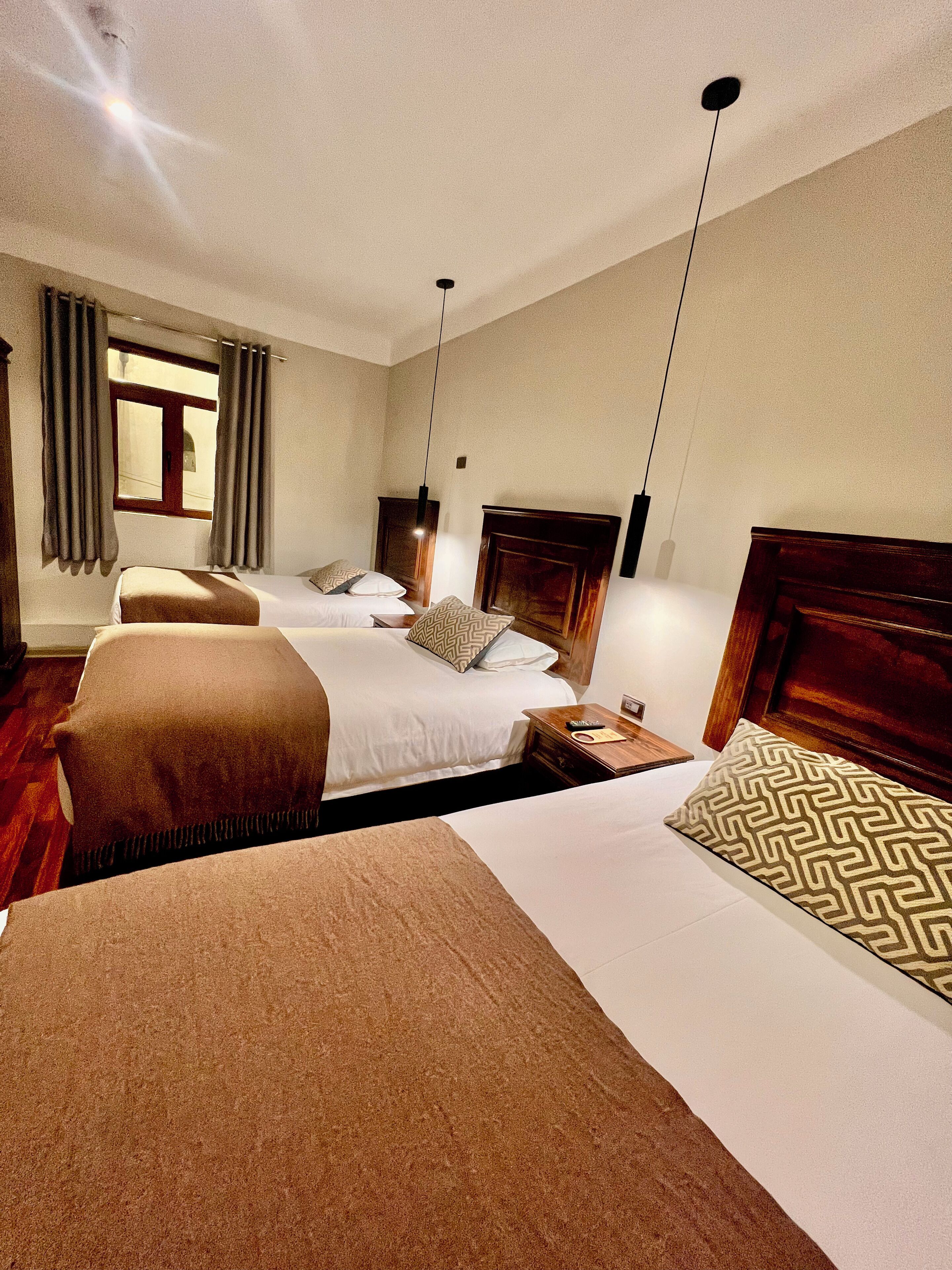 A hotel room with three beds, a wooden headboard, a window with curtains, and a ceiling fan.