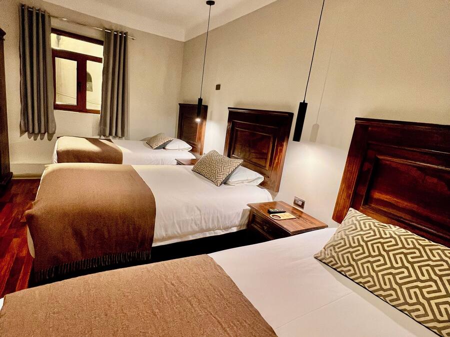 A hotel room with three beds, a wooden headboard, a window with curtains, and a ceiling fan.