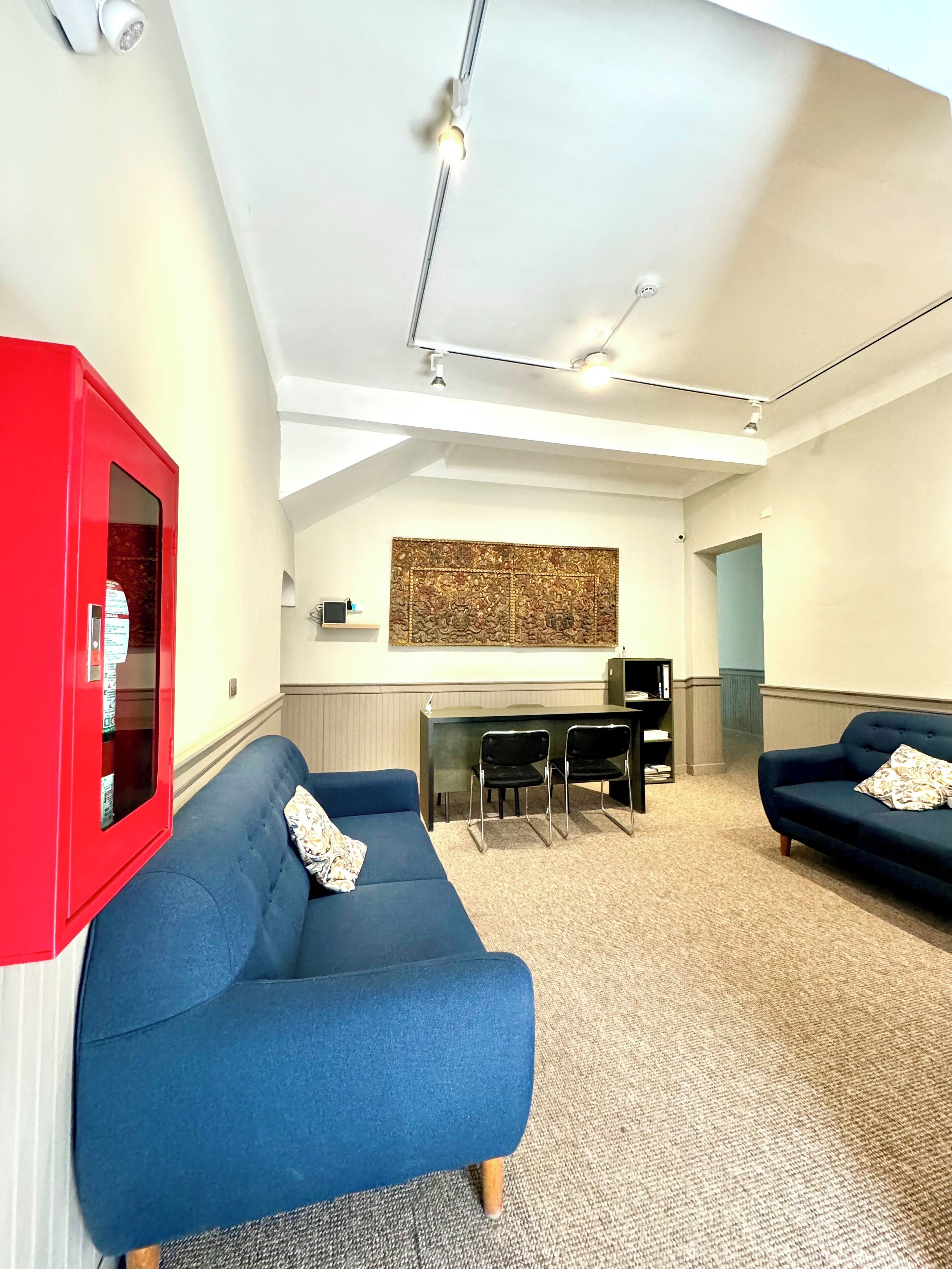 Uma sala de estar moderna com um sofá azul, um armário vermelho e uma área de jantar com uma mesa e cadeiras pretas.