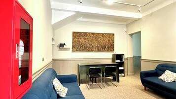 Uma sala de estar moderna com um sofá azul, um armário vermelho e uma área de jantar com uma mesa e cadeiras pretas.
