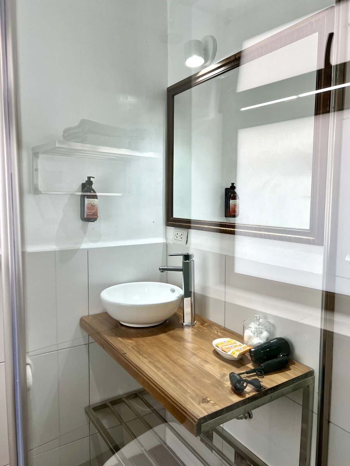 Ein modernes Badezimmer mit einem weißen Aufsatzwaschbecken, einem Holzwaschtisch, einer Glasdusche und einem Spiegel mit schwarzem Rahmen.