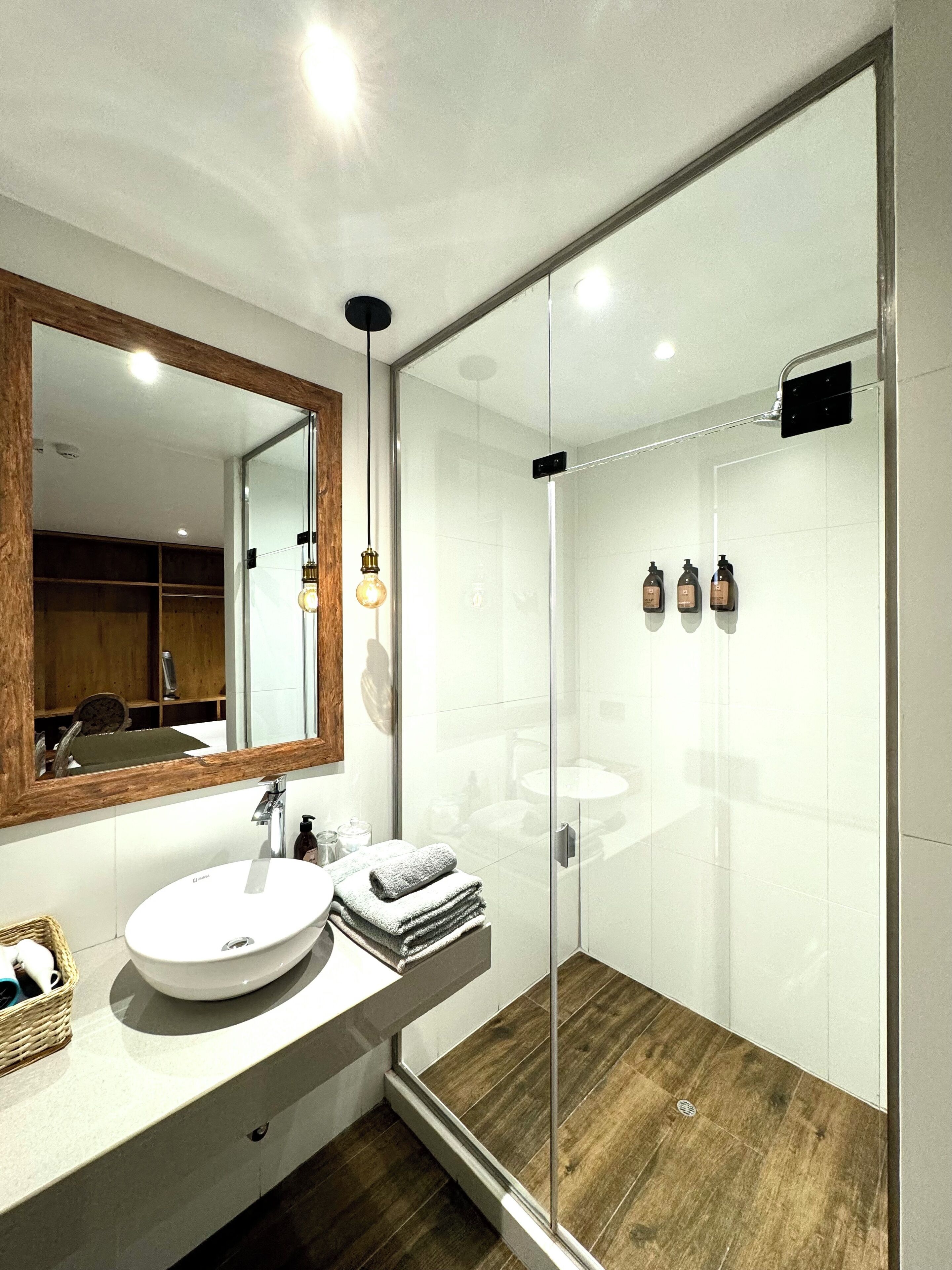 A modern bathroom with a glass shower enclosure, a large mirror, and a wooden vanity.