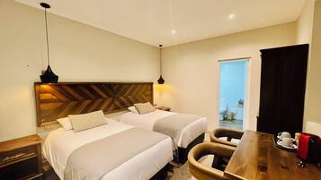 A hotel room with two beds, a wooden headboard, a desk with chairs, and a view of the bathroom.