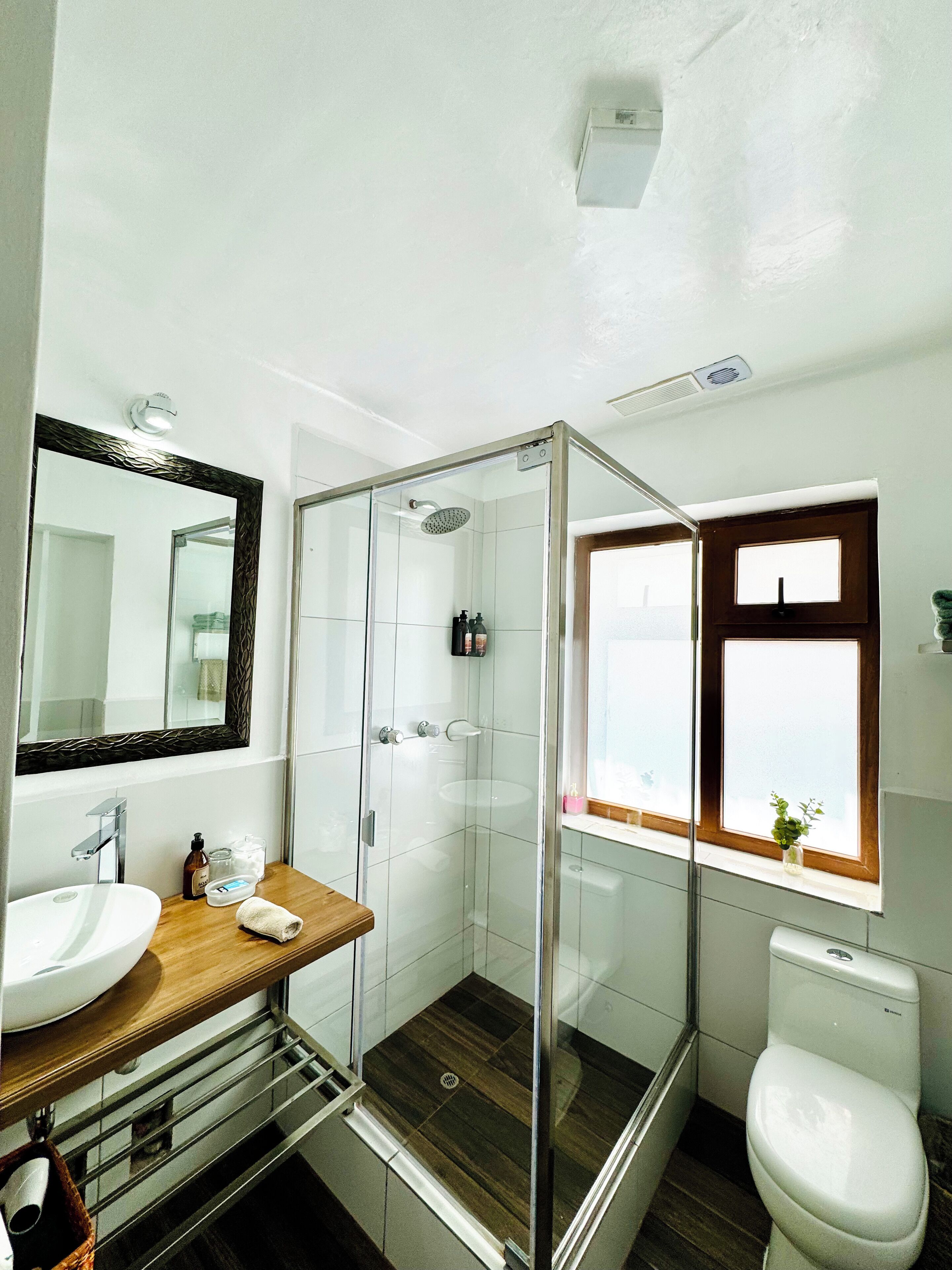 Un baño moderno con ducha envuelta en vidrio, un espejo grande, un lavamanos y un inodoro.