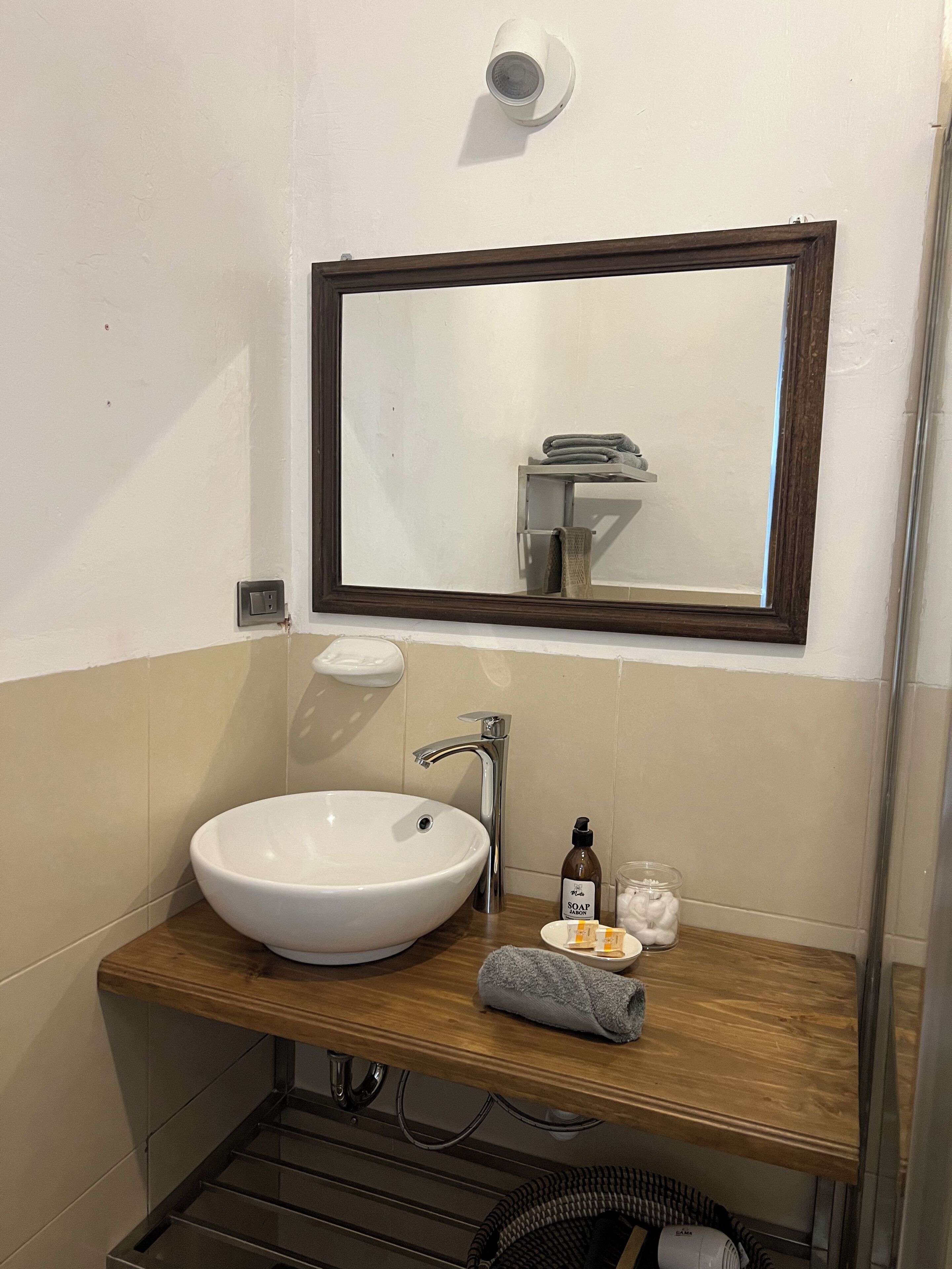 A bathroom with a white sink, a wooden countertop, a mirror with a dark frame, a towel, and a soap dispenser.