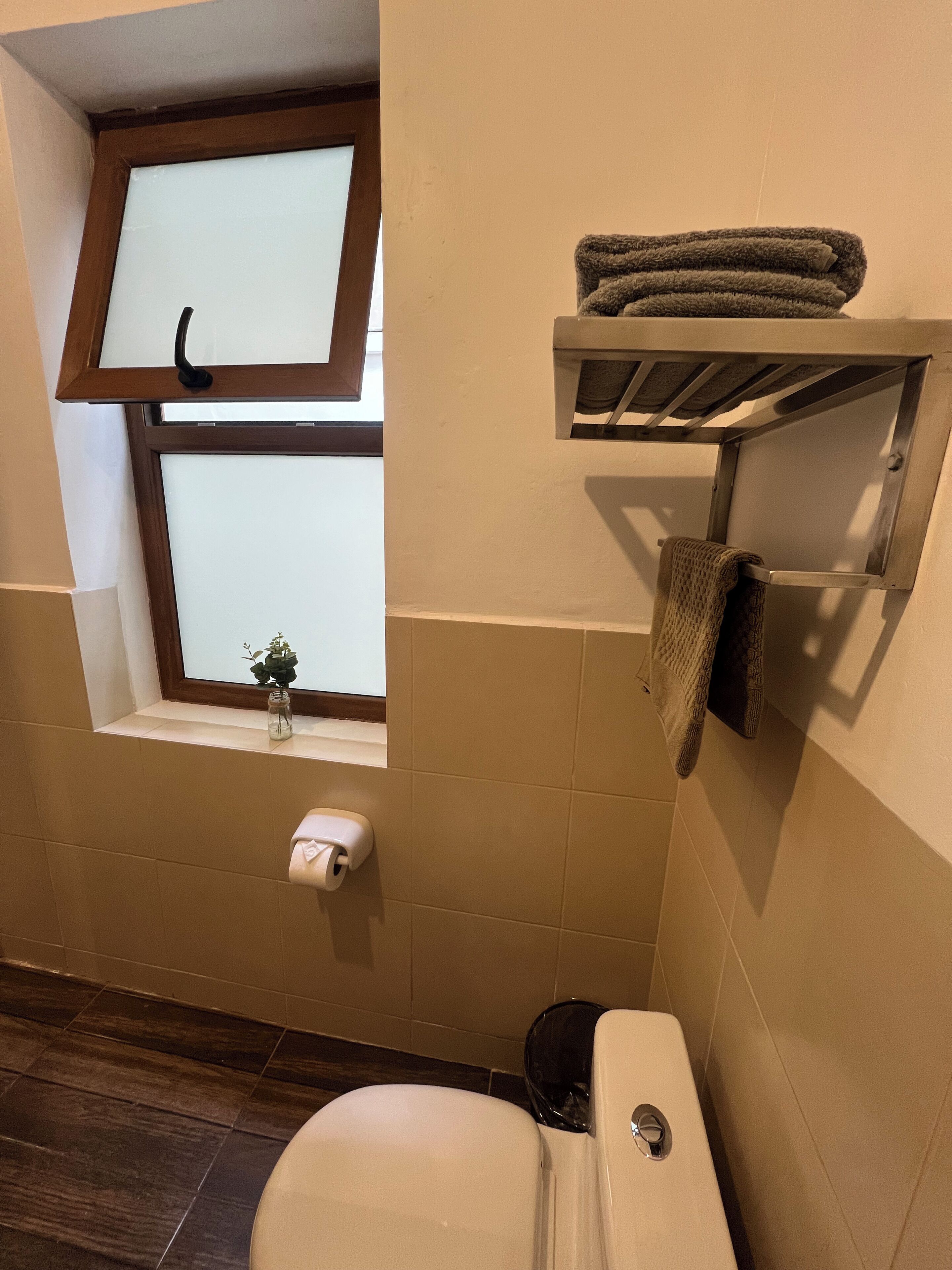 A bathroom with a toilet, a towel rack, a window, and a small shelf.