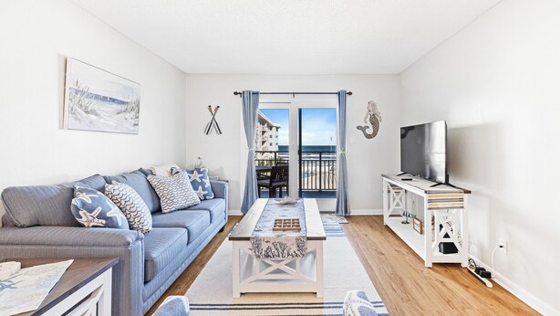 Un salon comprenant un canapé, une table basse, un téléviseur et offrant une vue sur la mer depuis un balcon.