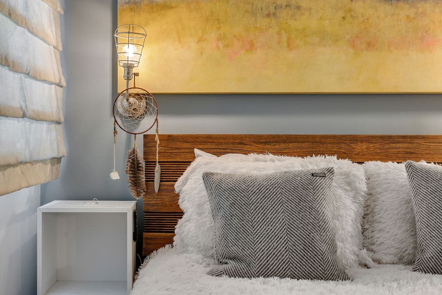 Un dormitorio con cabecera de madera, cubrecama blanco y esponjoso, y un atrapasueños con plumas.