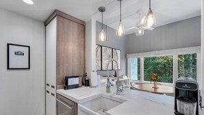 A modern kitchen with a built-in dishwasher, a coffee maker, and a large window offering a view of the outdoors. - Bridges Cozy Hideaway at Sugarbush (Warren)