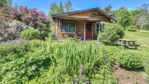 A rustic cabin with a wooden exterior, a red door, and a small porch. - VT Guest Cottage at Sugarbush in Moretown, VT (Northfield)