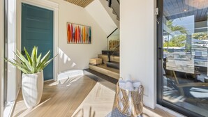 Un intérieur moderne avec un plancher en bois, une plante en pot, un escalier et une porte en verre donnant sur un espace extérieur.